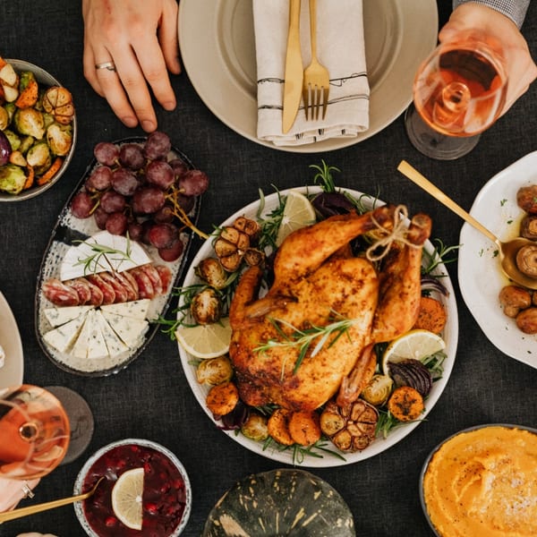 Overhead view of a roasted chicken dinner with sides of grapes, cheese, and vegetables.