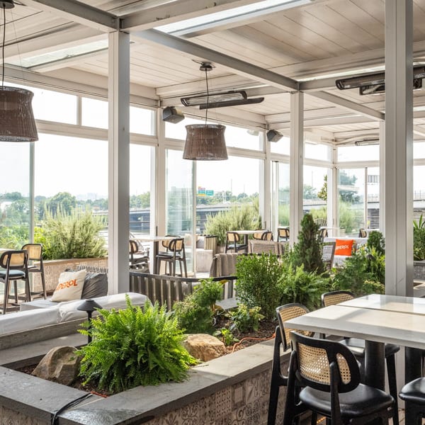 Officina's bright, airy rooftop patio with lush greenery, modern seating, and large windows overlooking the city.
