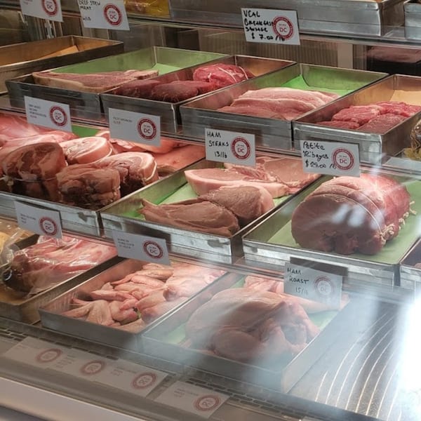 A refrigerated display case at Officina filled with various cuts of raw meat, including steaks, roasts, and sausages.