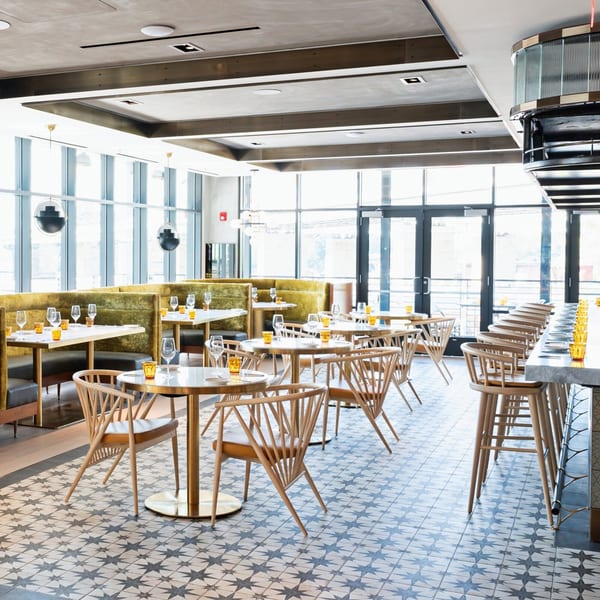 Officina's dining room features green velvet booths, light wood chairs, and star-patterned floor tiles.