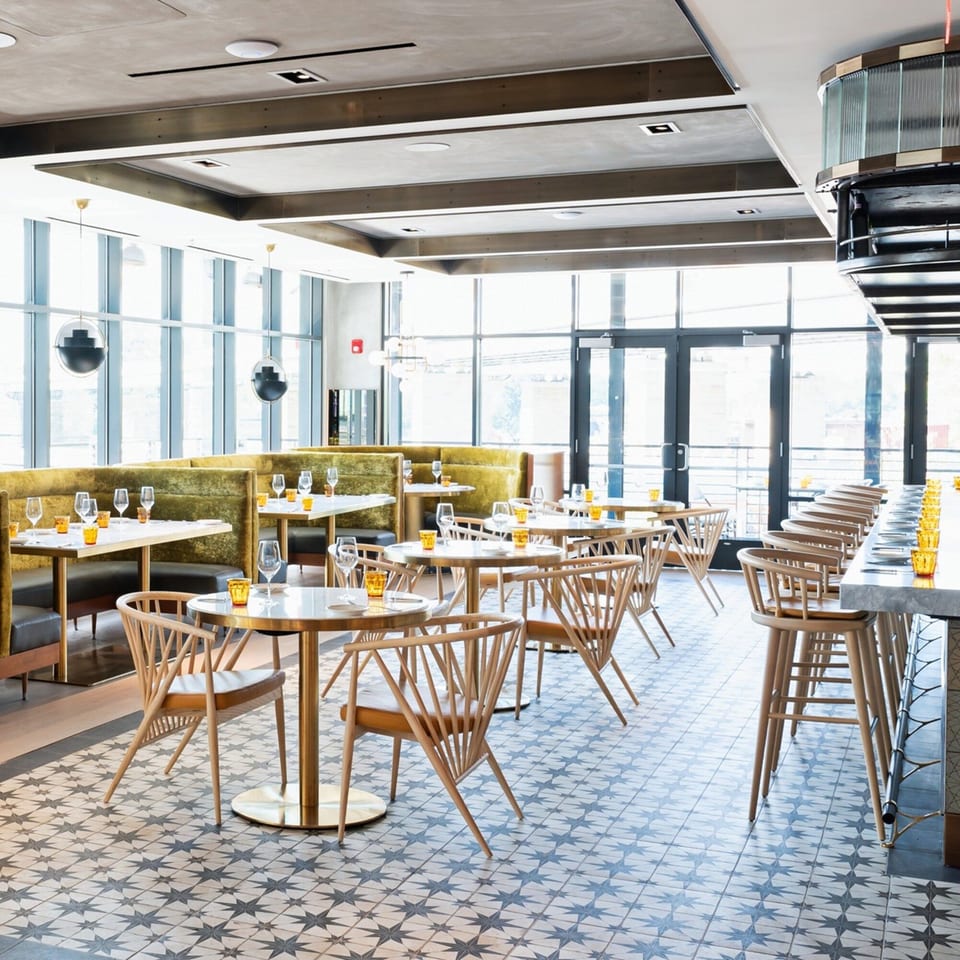 Officina's dining room features green velvet booths, light wood chairs, and star-patterned floor tiles.