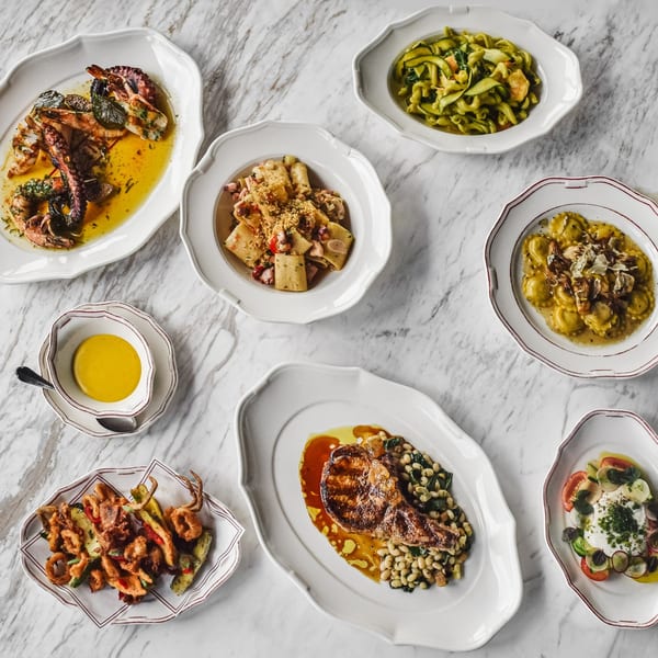 An overhead shot of seven different Italian dishes, including pasta, seafood, and meat, on a marble table.