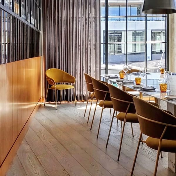 Long dining table set with glasses and plates, surrounded by mustard yellow chairs in a modern Officina dining room.