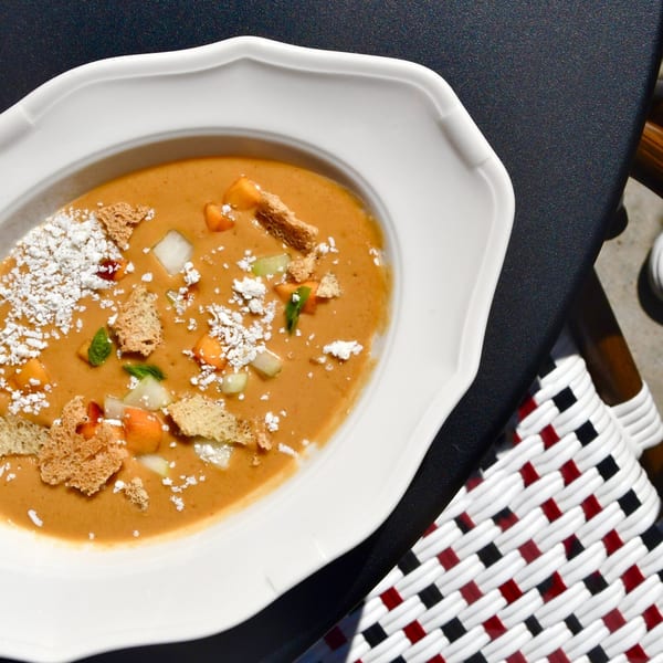 A bowl of Officina's Italian soup with croutons, cheese, and vegetables on a dark table.