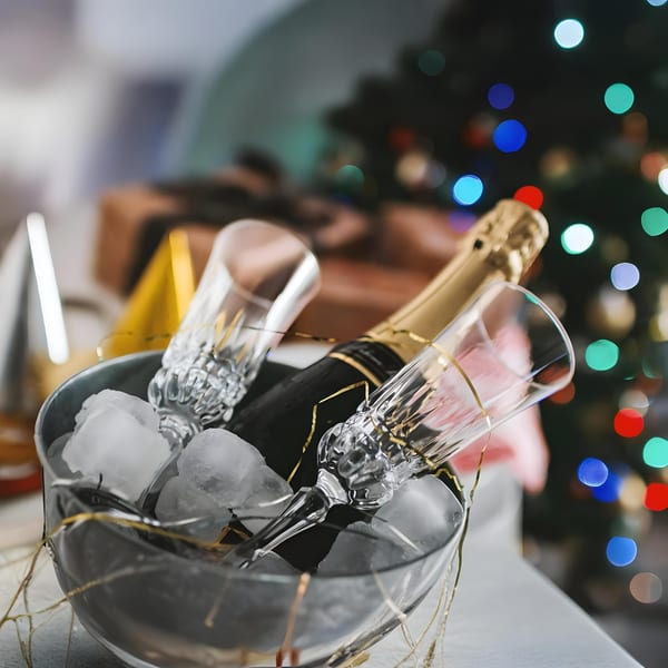 Champagne bottle and two flutes in an ice bucket, with festive lights in the background.