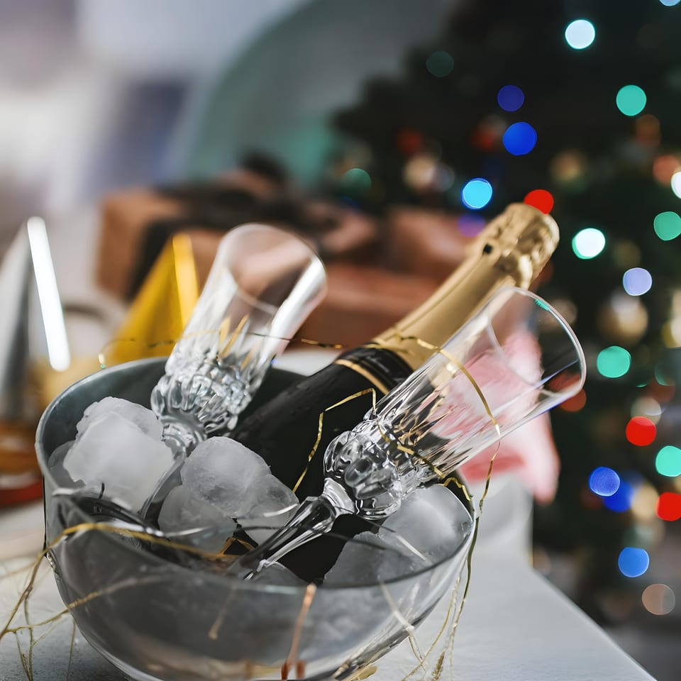 Champagne bottle and two flutes in an ice bucket, with festive lights in the background.