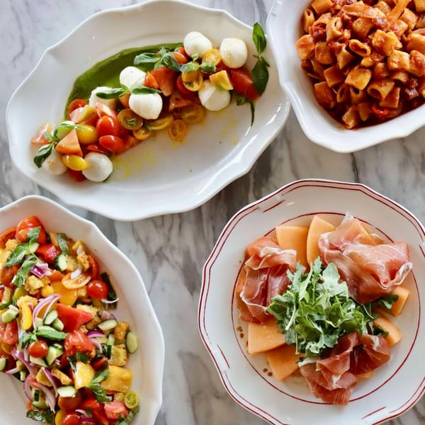 Four Italian dishes: Caprese salad, pasta, panzanella, and prosciutto with melon on a marble table.