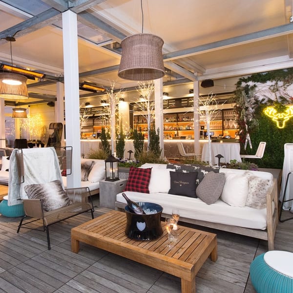 Officina's outdoor lounge area with sofas, chairs, a wooden table with champagne, and a bar in the background.