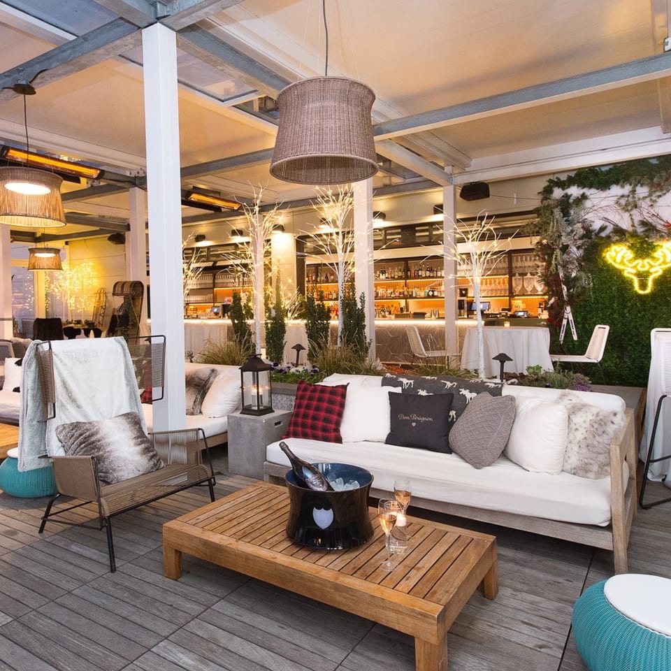Officina's outdoor lounge area with sofas, chairs, a wooden table with champagne, and a bar in the background.