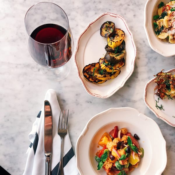 Overhead view of Italian dishes: grilled zucchini, pasta, salad, and a glass of red wine.