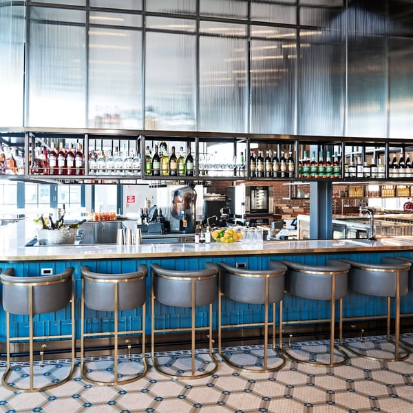 A long, well-stocked bar with blue tiled front, gray stools, and a patterned floor at Officina.