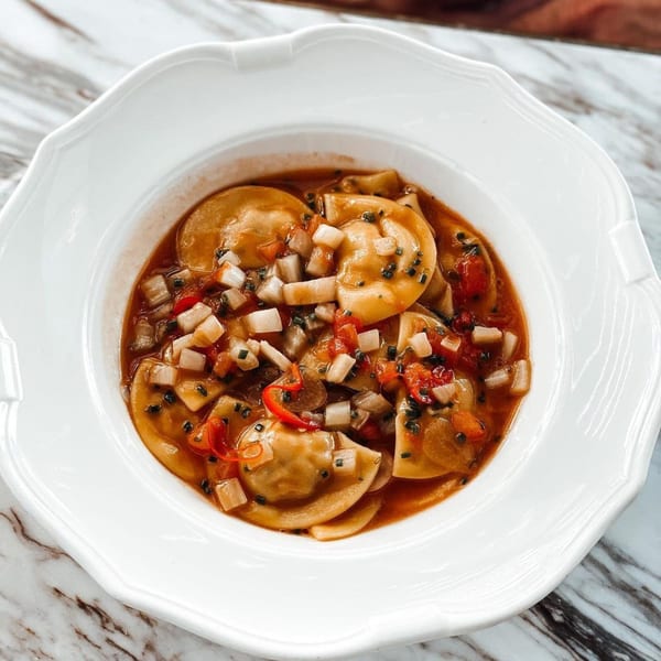 Officina's ravioli in a rich sauce with diced vegetables and black sesame seeds in a white bowl.