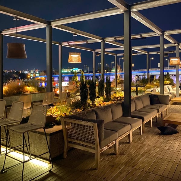 Officina's rooftop patio at night, featuring lounge seating, bar stools, and city lights in the background.