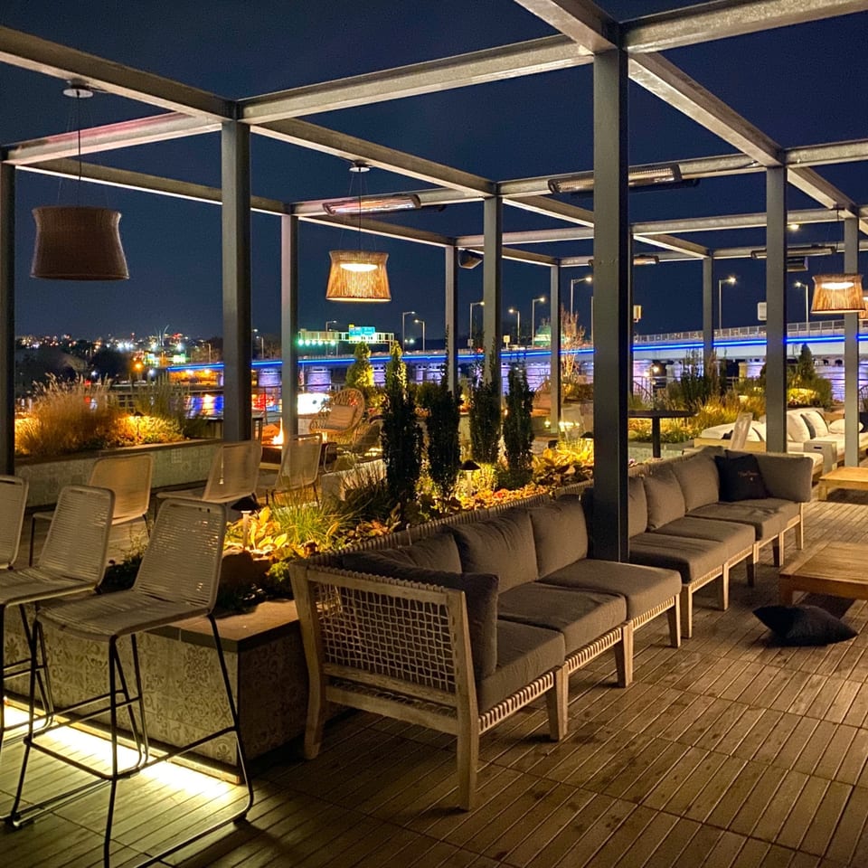 Officina's rooftop patio at night, featuring lounge seating, bar stools, and city lights in the background.