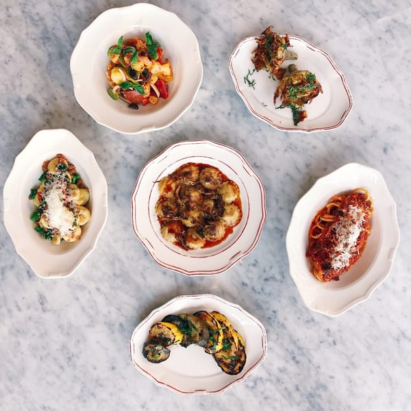 Six Italian dishes, including pasta, gnocchi, and grilled vegetables, arranged on a marble table.