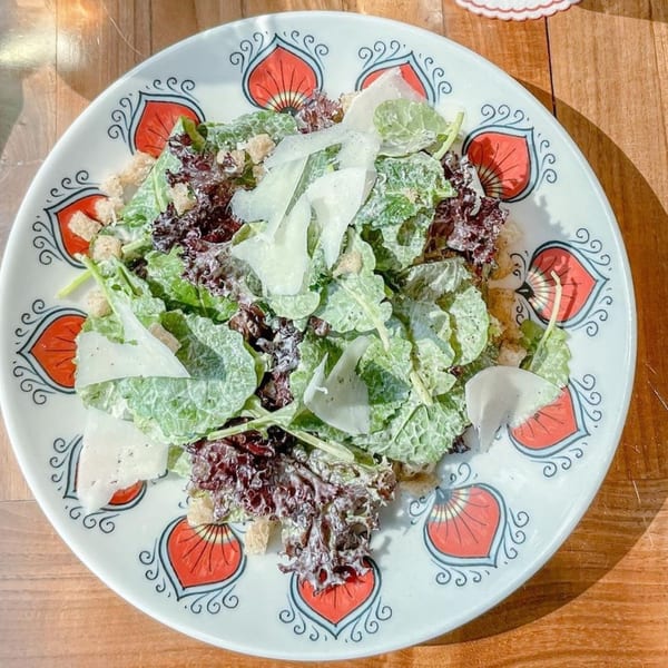 Officina's Caesar salad with mixed greens, croutons, shaved parmesan, and creamy dressing on a decorative plate.