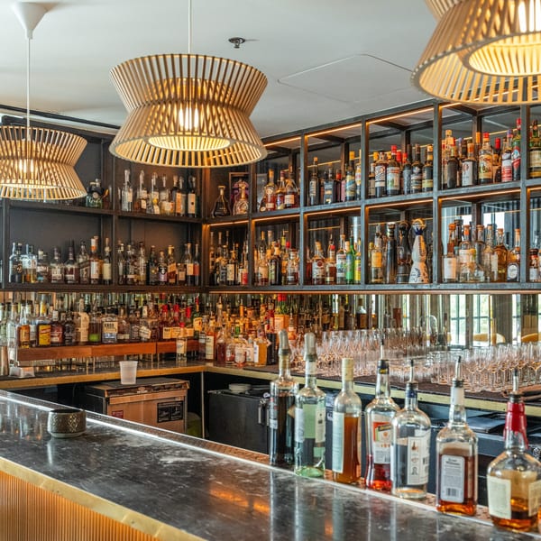 A well-stocked bar at Officina, featuring numerous liquor bottles on shelves and a marble countertop.
