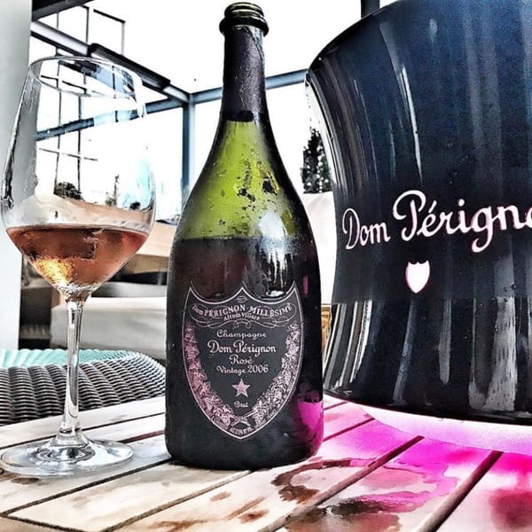 A bottle of Dom Pérignon Rosé 2006 champagne and a glass of rosé on a wooden table.