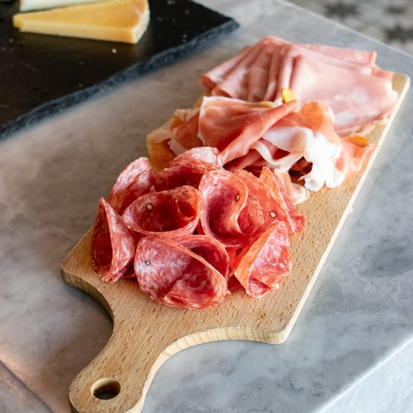 A wooden board with an assortment of Italian cured meats, including salami, prosciutto, and mortadella.
